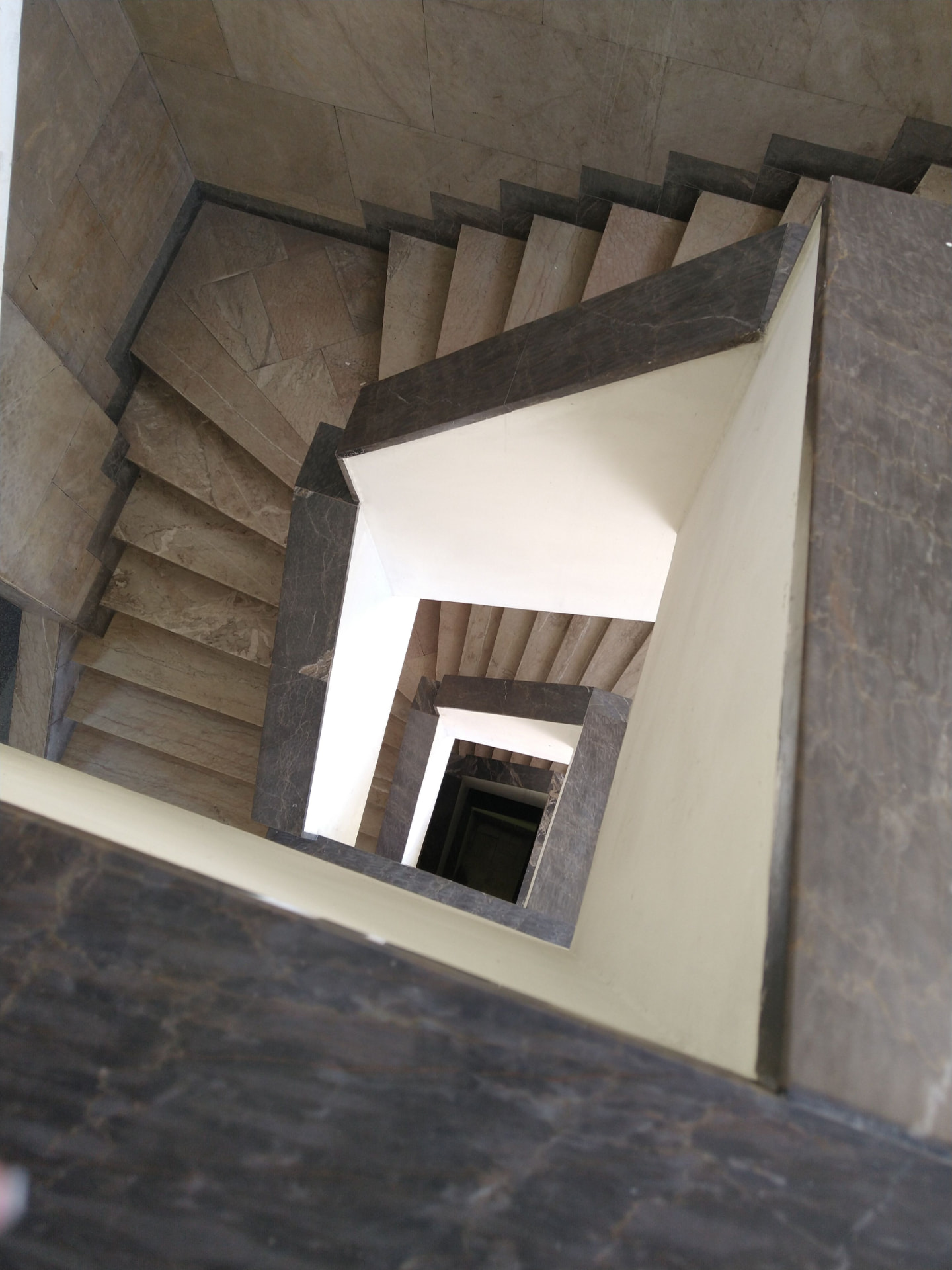 Escada espiral quadrada em mármore vista de cima, com degraus em torno do vazio central.
