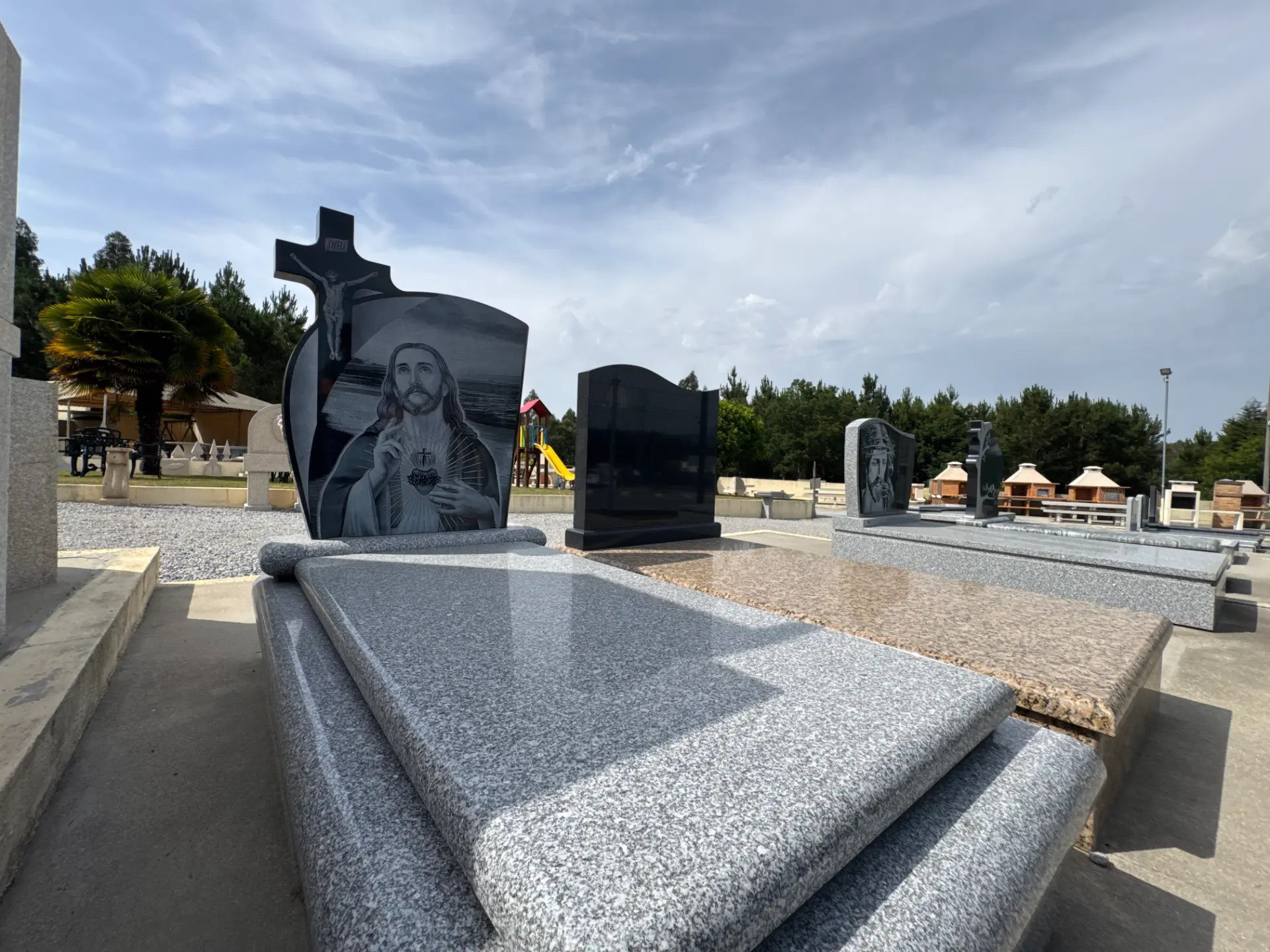 Campas de família em granito polido com gravações religiosas, num cemitério ajardinado.