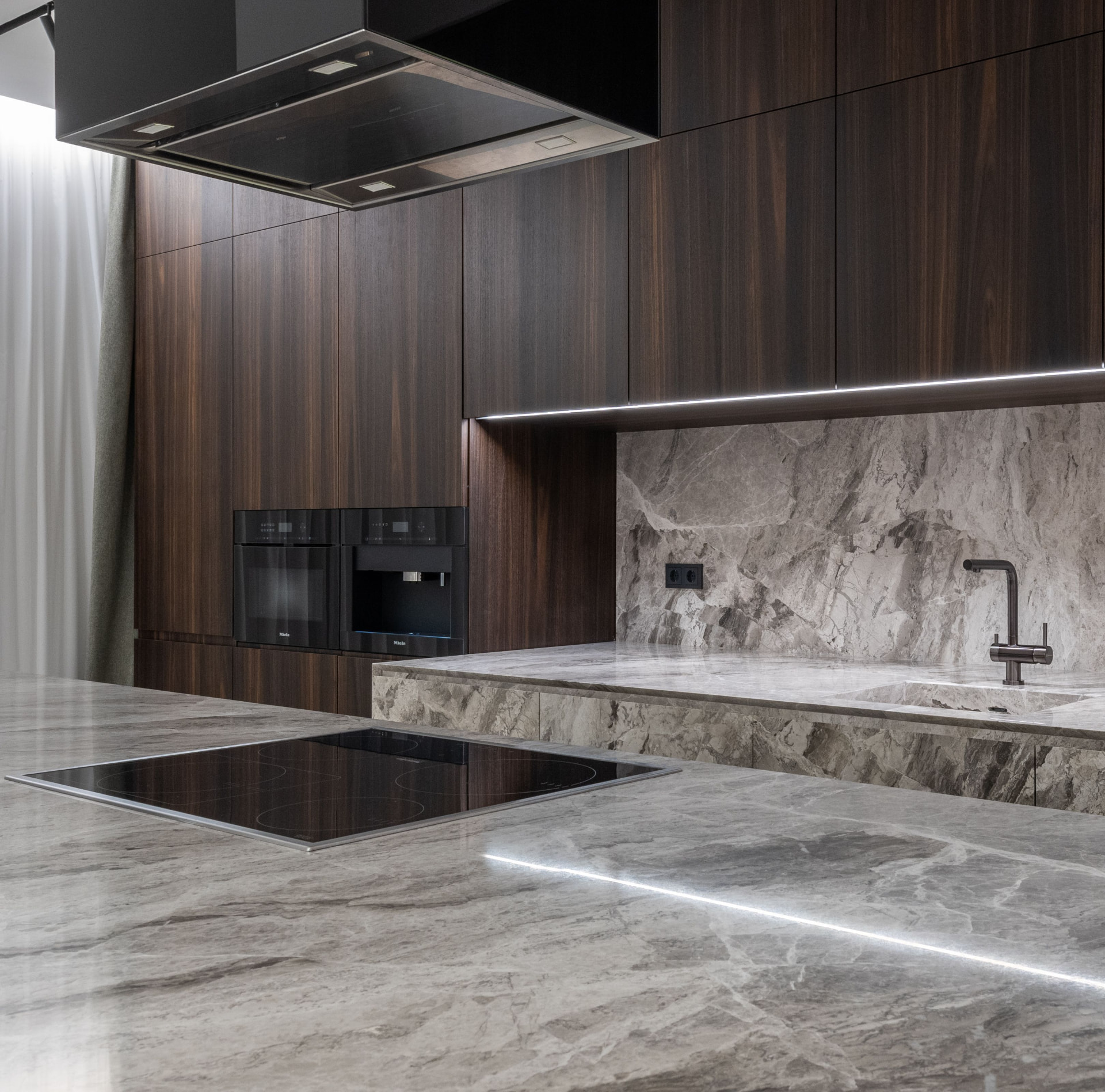 Bancada e painel de cozinha em pedra natural cinzenta com iluminação integrada sob os armários.