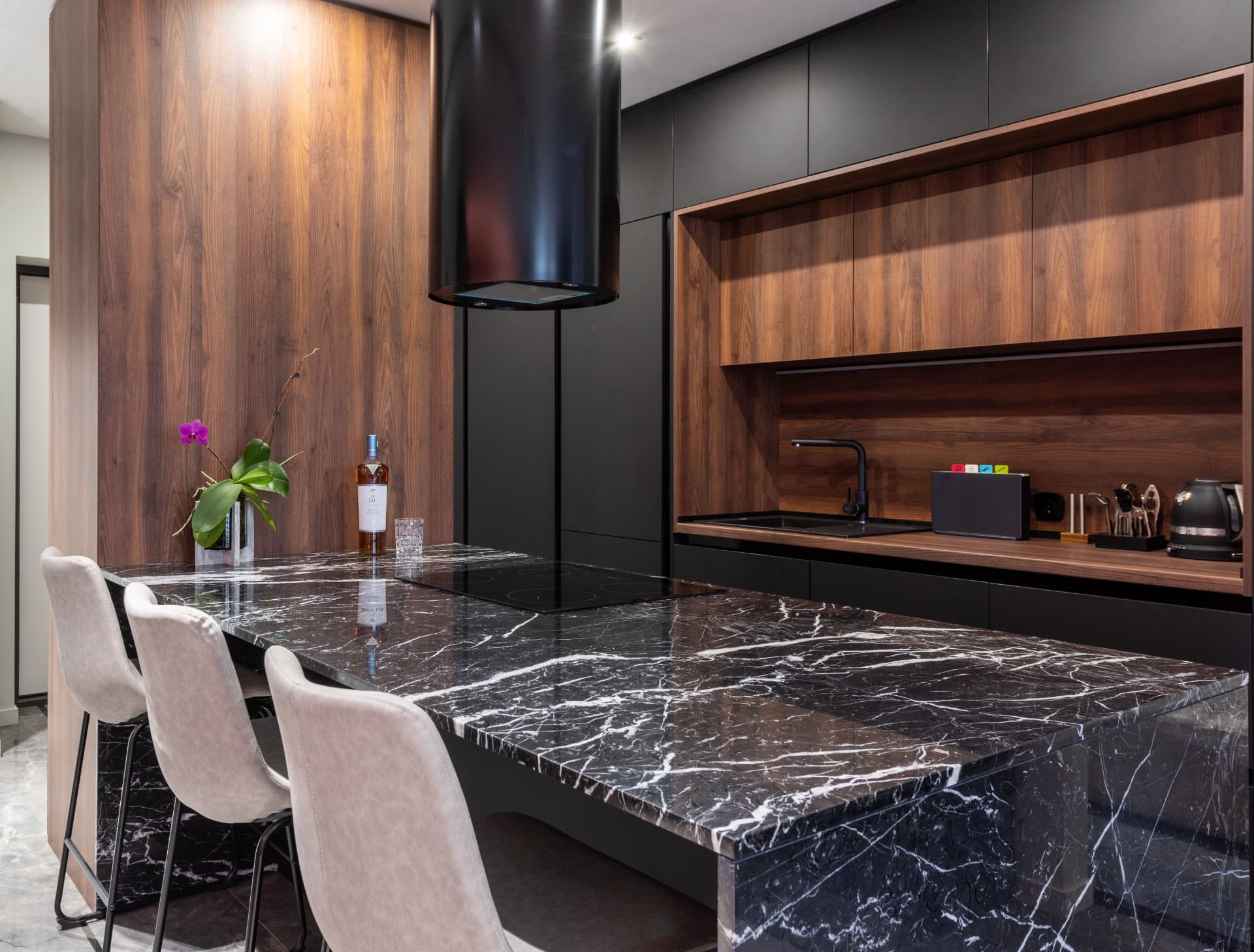 Ilha de cozinha em mármore preto com veios brancos, banqueta e mobiliário em madeira escura.