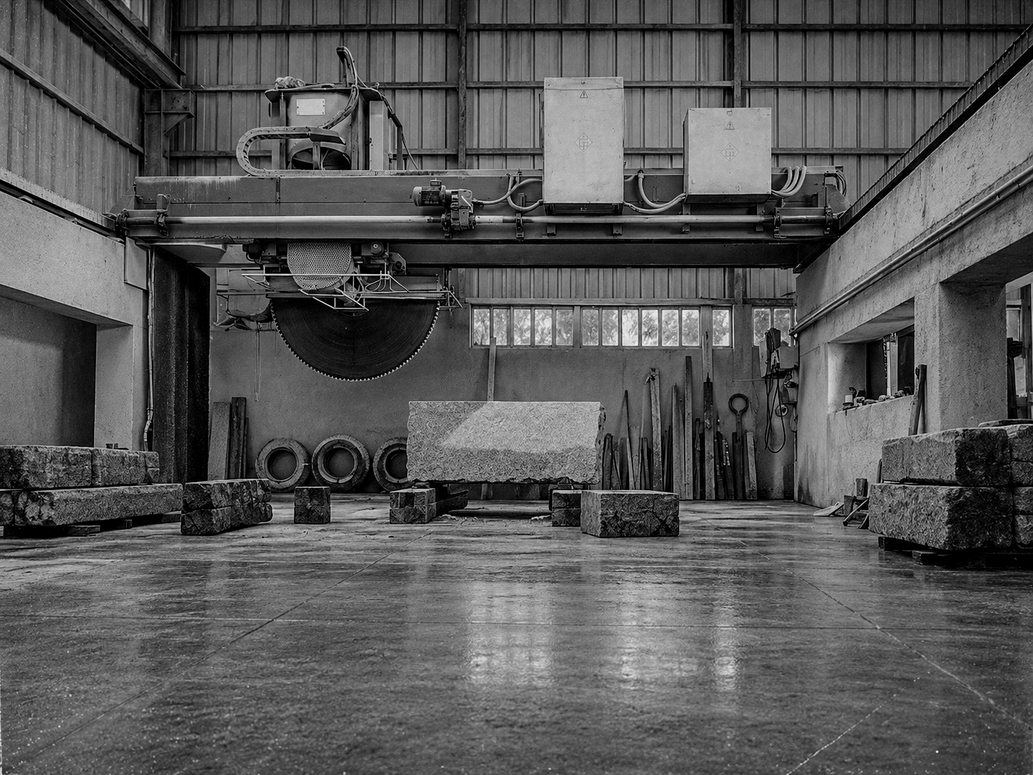Máquina de corte industrial tipo ponte, em preto e branco, com blocos de pedra na zona de transformação das instalações da Granineiva.