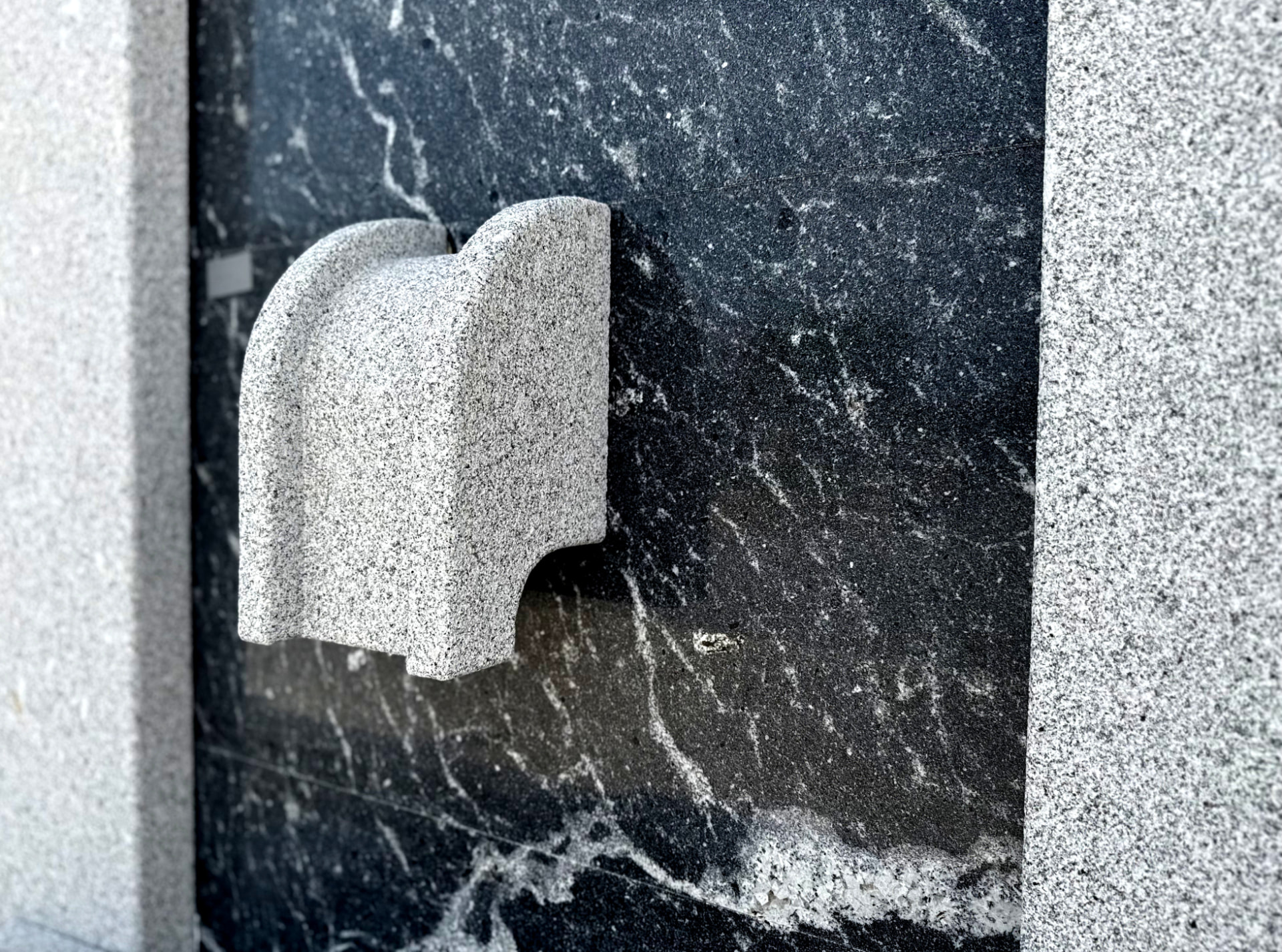 Fonte em granito cinzento montada numa parede revestida a mármore preto e branco.