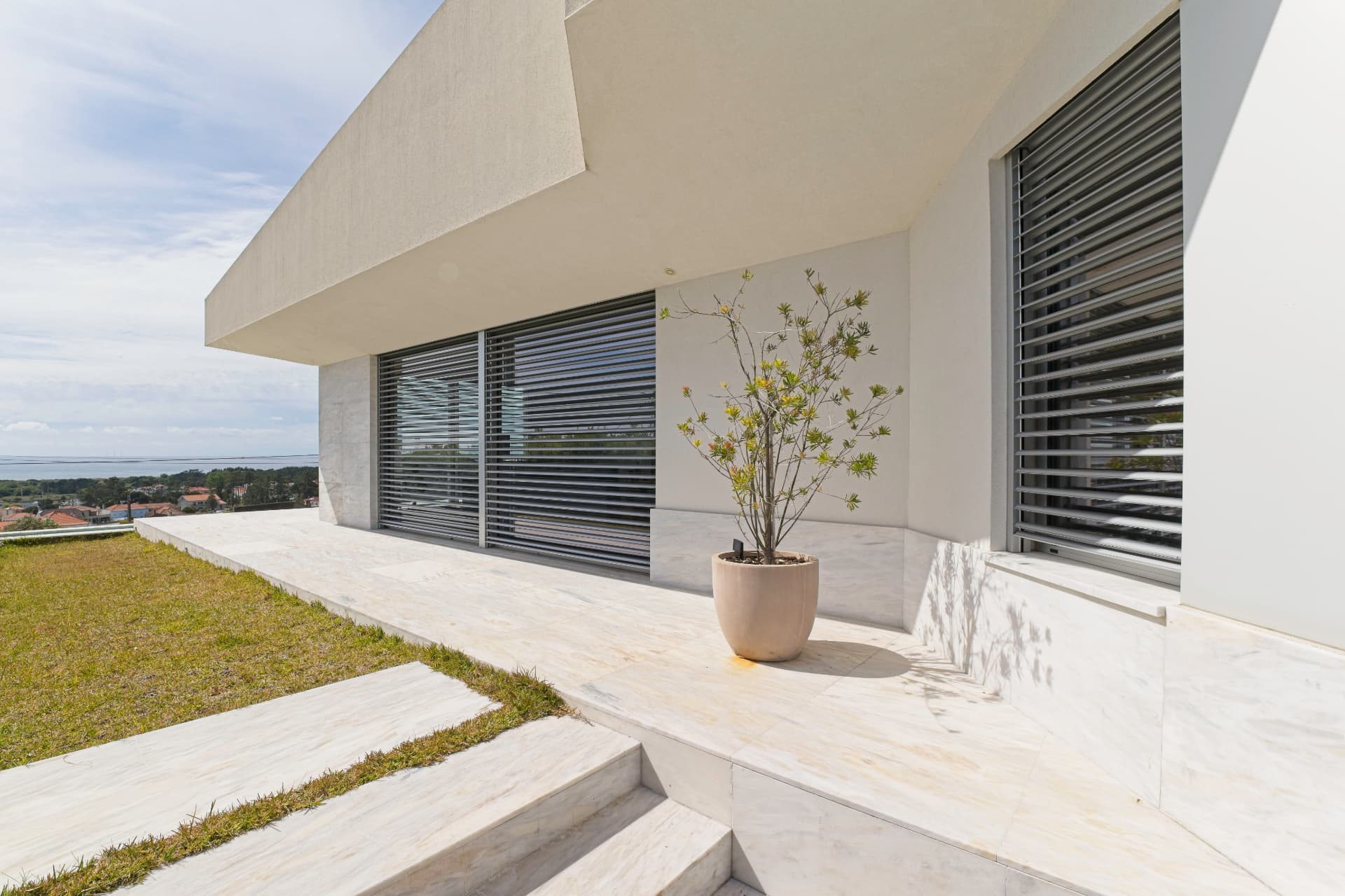 Varanda de habitação contemporânea com pavimento e muretas em mármore claro e vasos ornamentais.