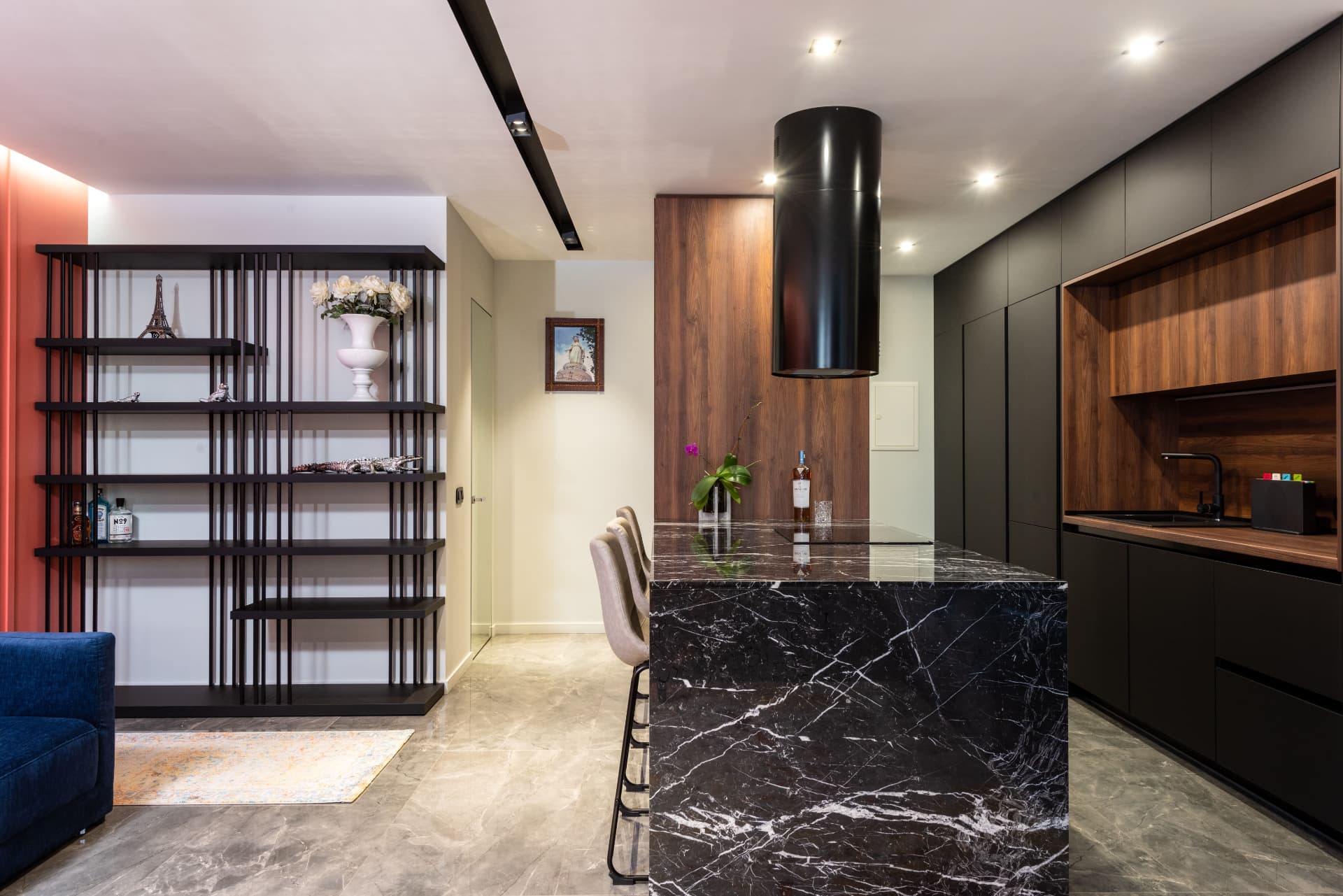 Cozinha contemporânea com ilha central em mármore preto, armários escuros e painel em madeira.